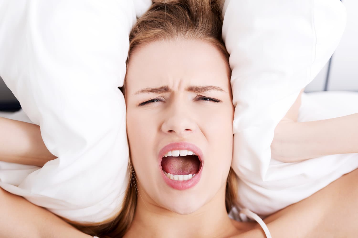women holding pillow over her ears and screaming